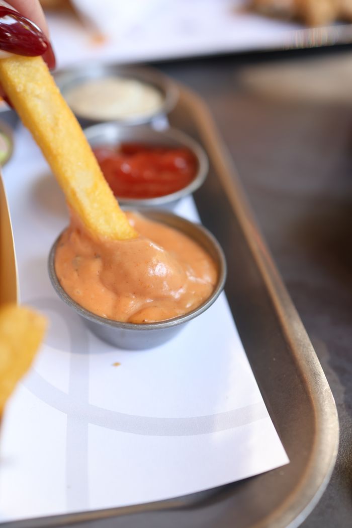 Close-up of a french fry being dipped into a creamy sauce with other condiments.